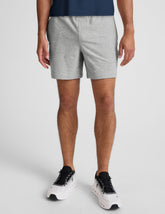 man wearing a navy t-shirt and gray shorts on a plain background.